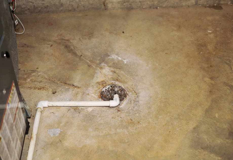a rusted basement drain, with PVC pip leading to it at a right angle 